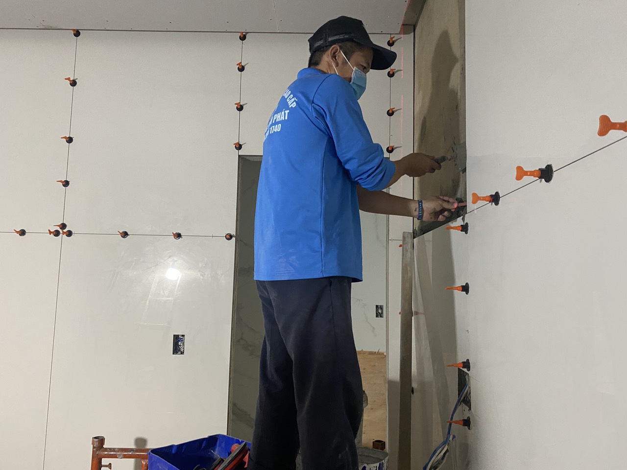 Thợ thi công đang sử dụng ke cân bằng để ốp gạch tường phẳng tắp.