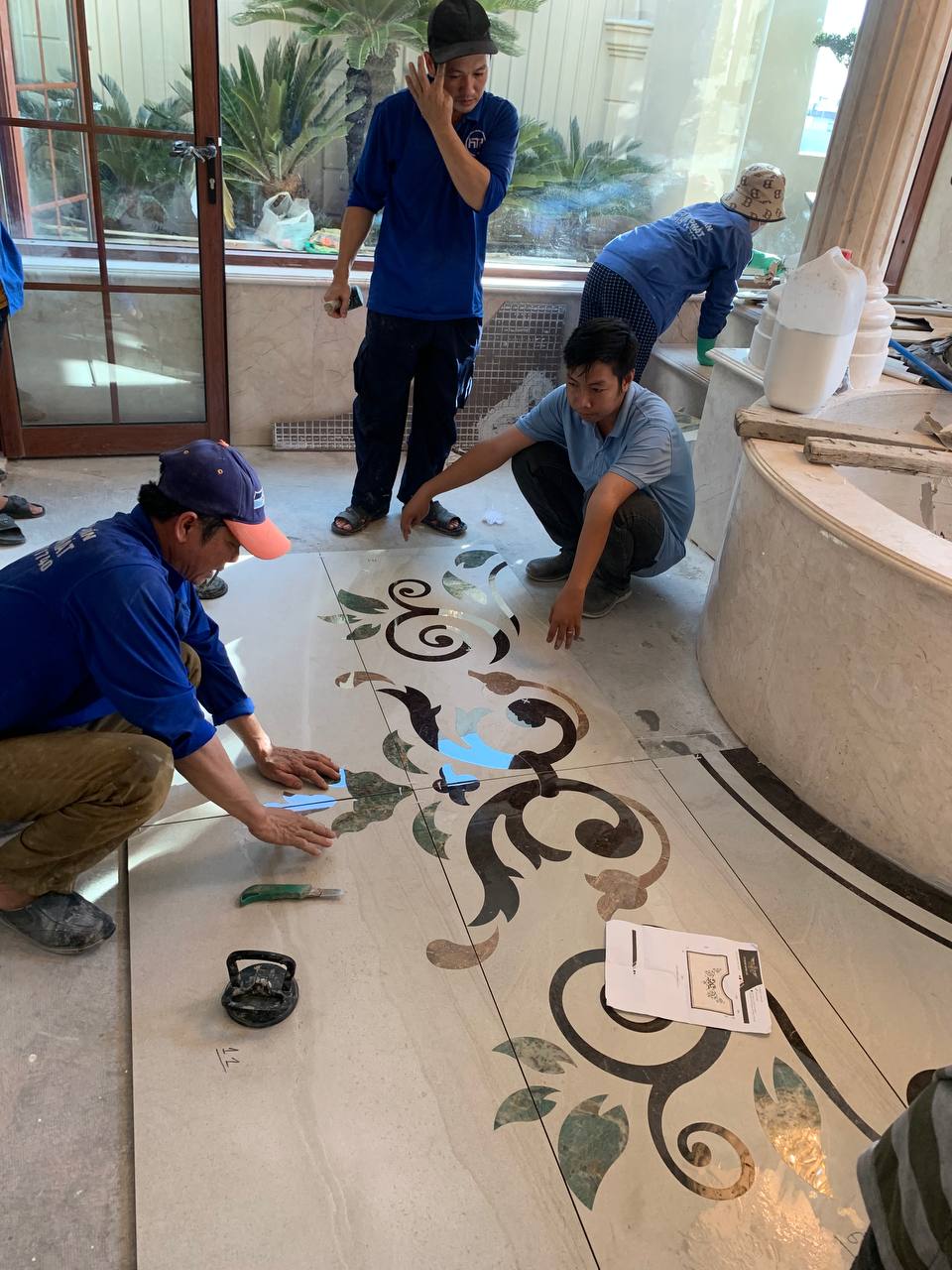 Đội ngũ thợ đang ghép tranh đá hoa văn cổ điển trên nền sàn.