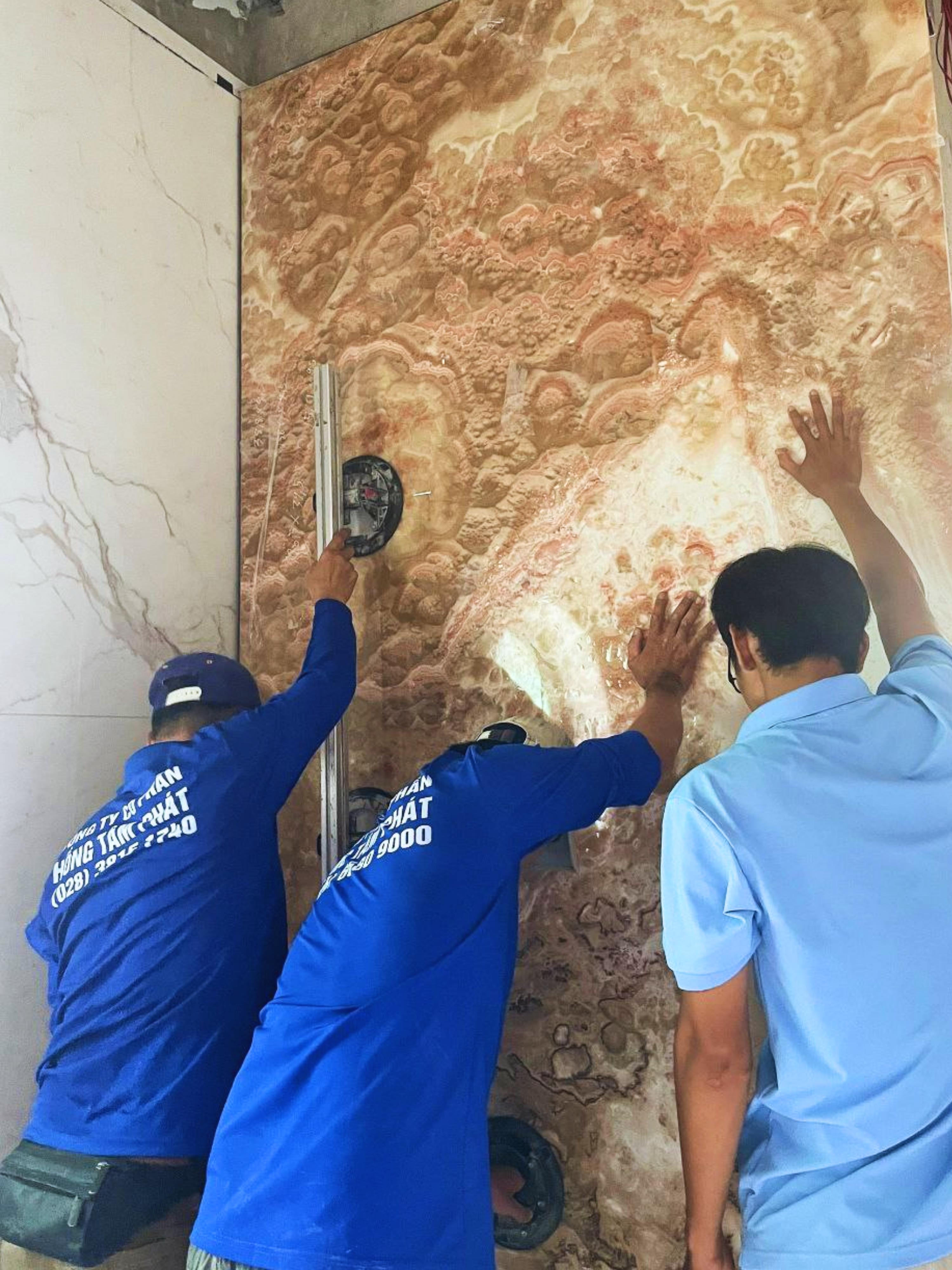 Đội thợ đang phối hợp lắp đặt tấm đá Onyx vàng vân gỗ khổ lớn.